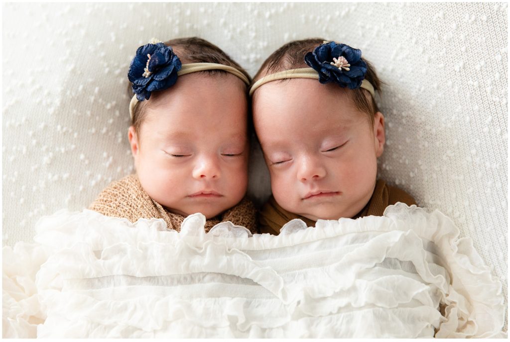 Twin girls snuggled under blanket blue bows